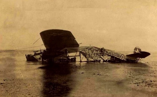 A crumpled, crashed aircraft in a body of water. America is written on the side of the aircraft.